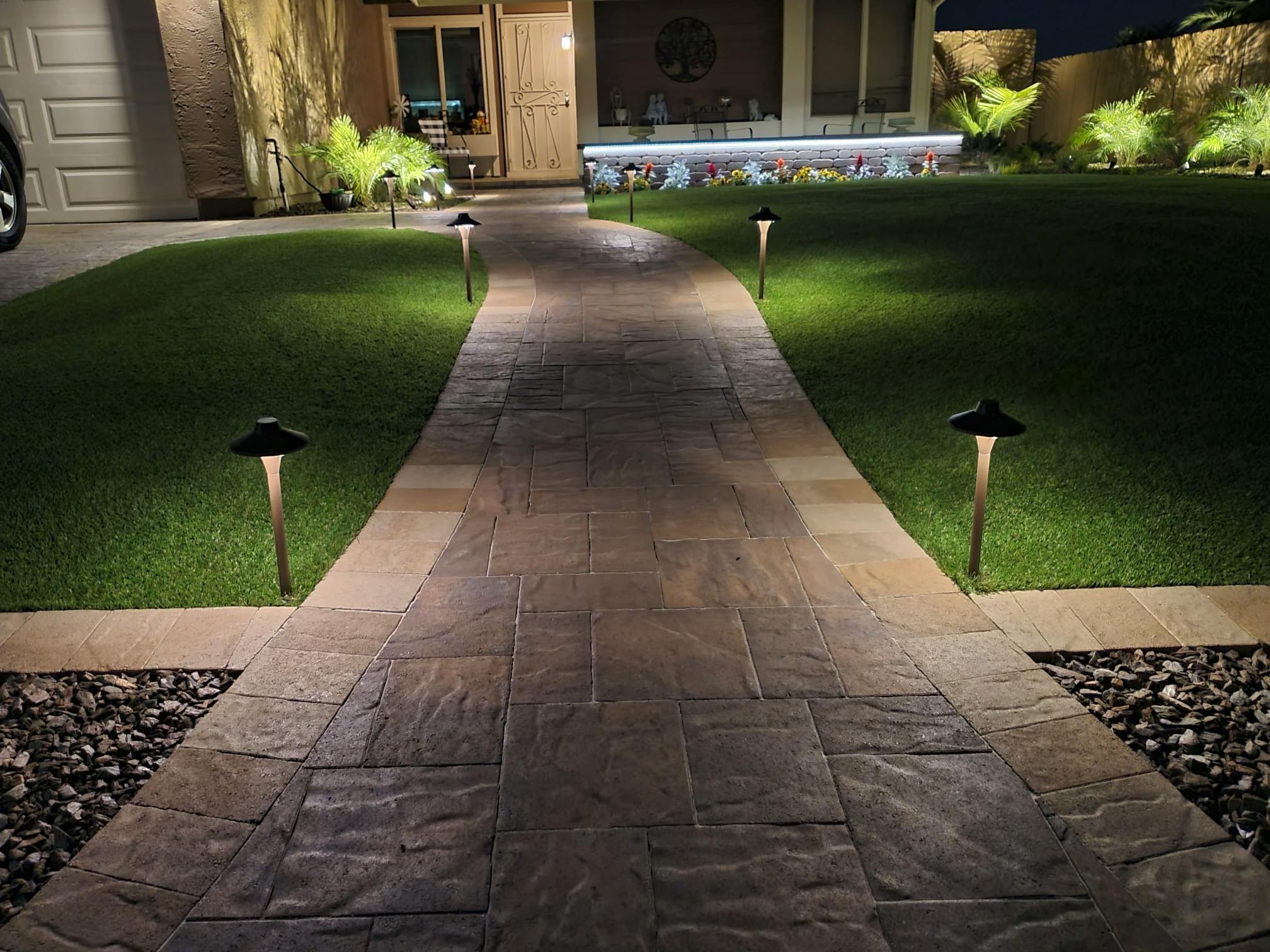 Photo of a backyard landscape with artificial turf and a hardscape walkway.